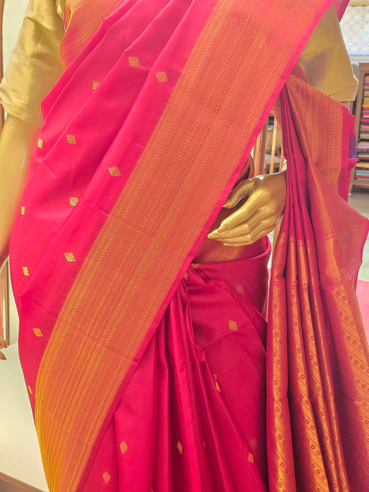 Rani pink silk saree adorned with a traditional golden zari border and small geometric butta motifs woven throughout the body