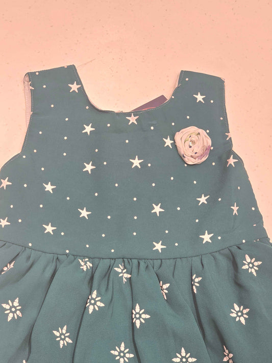 This teal cotton frock dress for girls features a classic dual-pattern design, with small white stars scattered across the sleeveless bodice and a geometric snowflake or floral print adorning the gathered A-line skirt. It