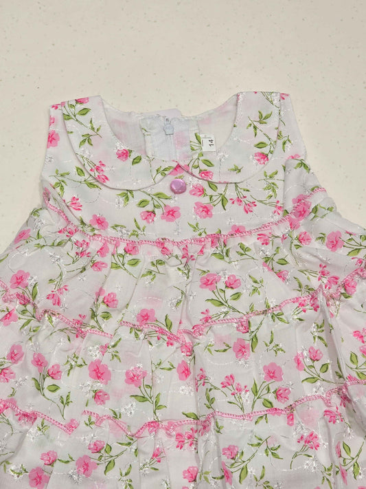 white baby girl's cotton frock dress featuring a vibrant pink floral print distributed in distinct tiered ruffle layers.