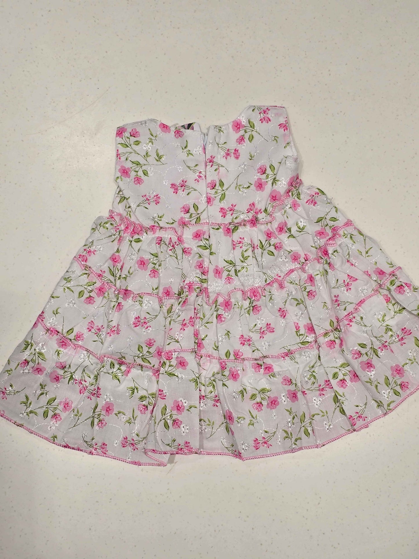white baby girl's cotton frock dress featuring a vibrant pink floral print distributed in distinct tiered ruffle layers.