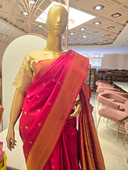 Rani pink silk saree adorned with a traditional golden zari border and small geometric butta motifs woven throughout the body