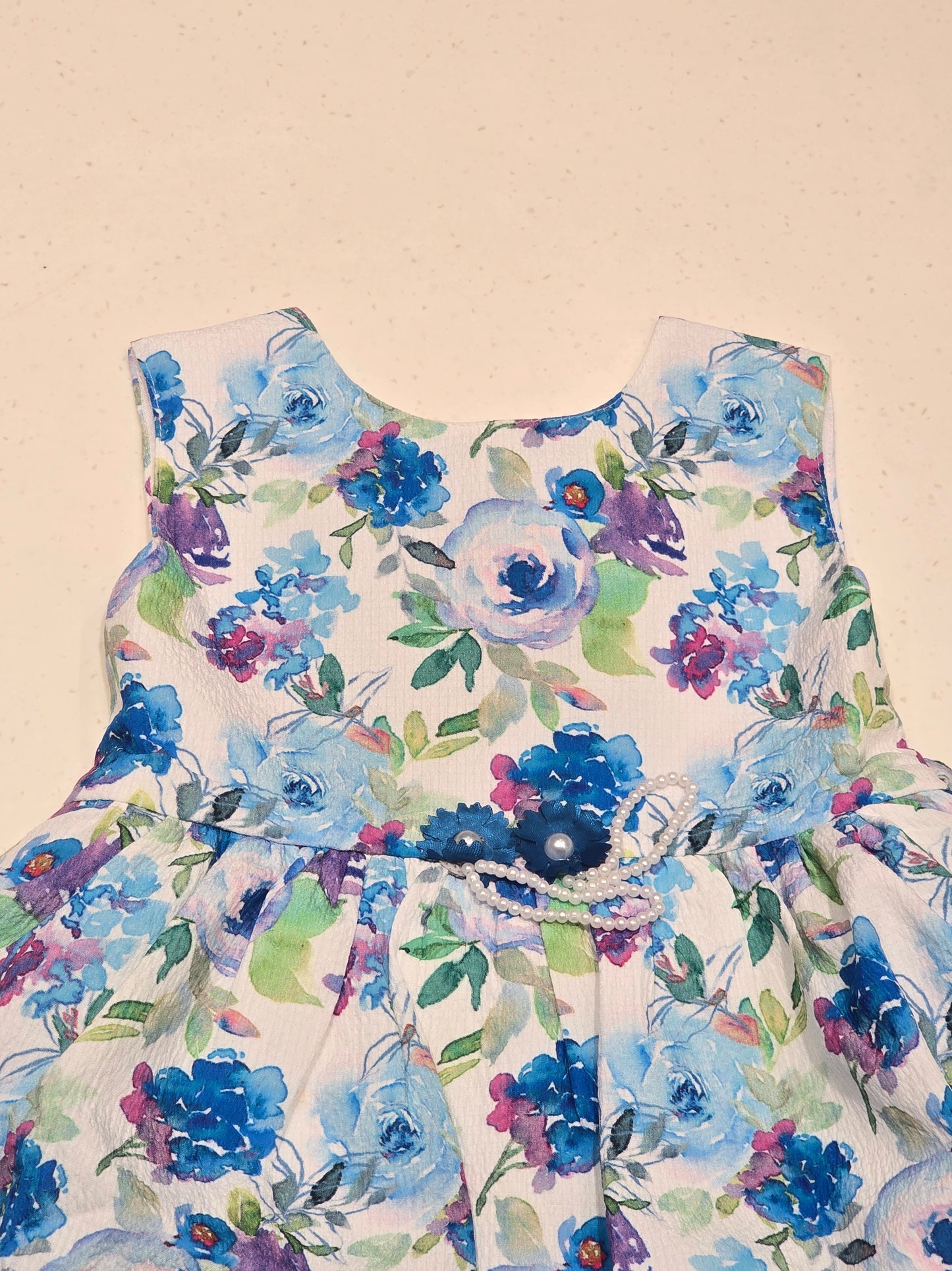baby girl sleeveless cotton frock featuring a vibrant blue, purple, and green watercolor floral print on a crisp white background.