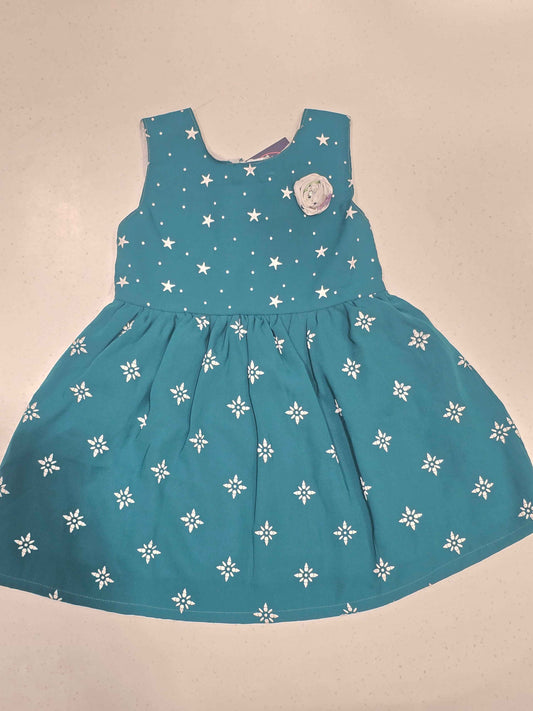 This teal cotton frock dress for girls features a classic dual-pattern design, with small white stars scattered across the sleeveless bodice and a geometric snowflake or floral print adorning the gathered A-line skirt. It