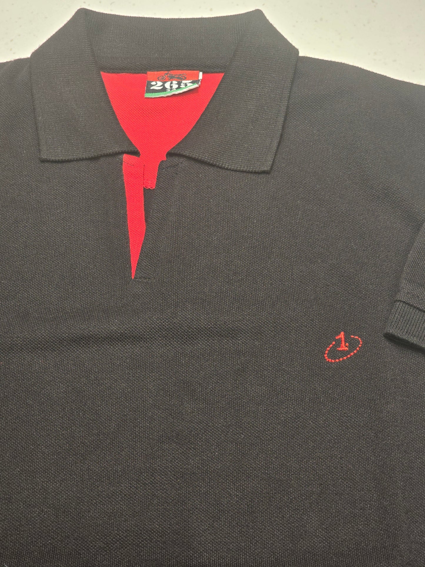 black or dark charcoal knit polo shirt featuring a red contrast inner placket and an embroidered chest logo