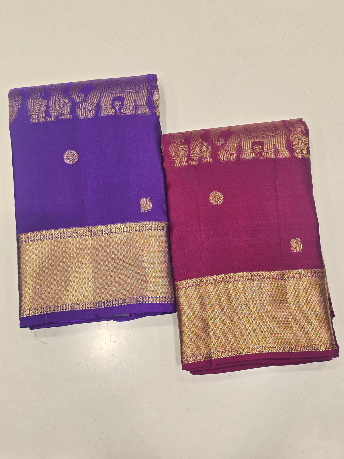 One saree is a deep royal purple, and the other is a rich magenta/wine tone.