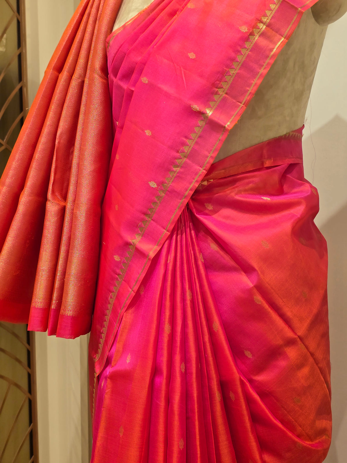 vibrant dual-tone pink and orange Kanchipuram silk saree elegantly draped on a mannequin.