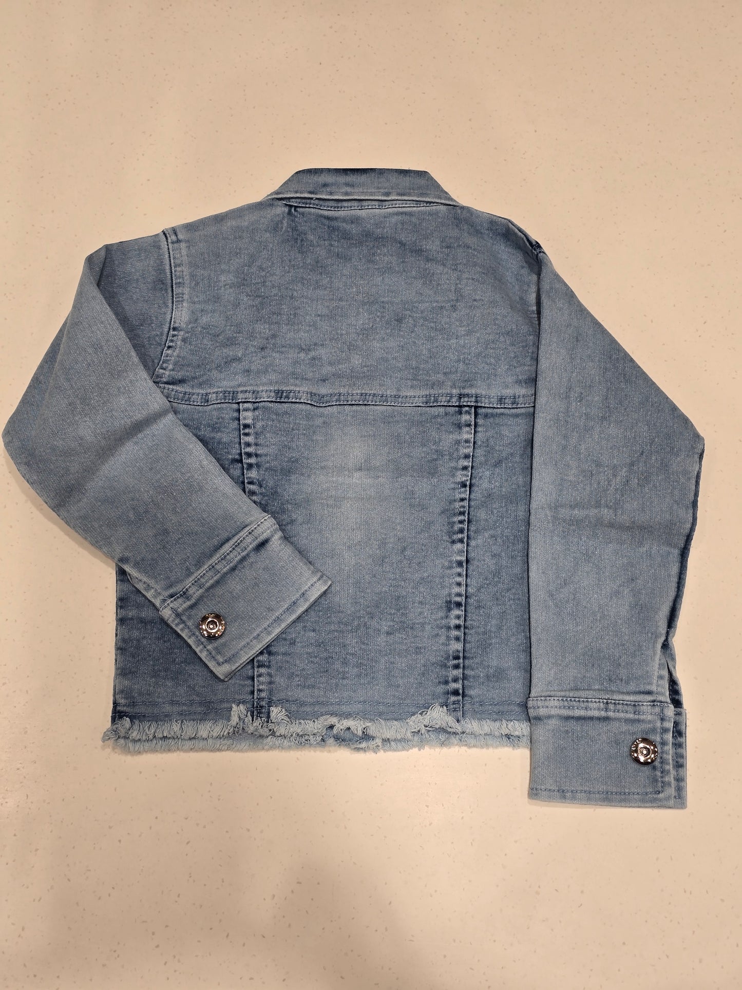 washed blue denim jacket featuring front flap pockets, a spread collar, custom decorative buttons, and a small embroidered chest patch.