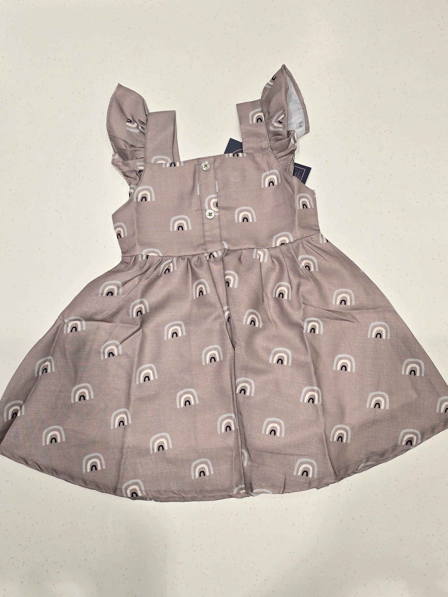 baby girl’s sleeveless cotton frock featuring a flared skirt, a gathered waist, square neckline, shoulder flutter ruffles, and a button-down back closure. It