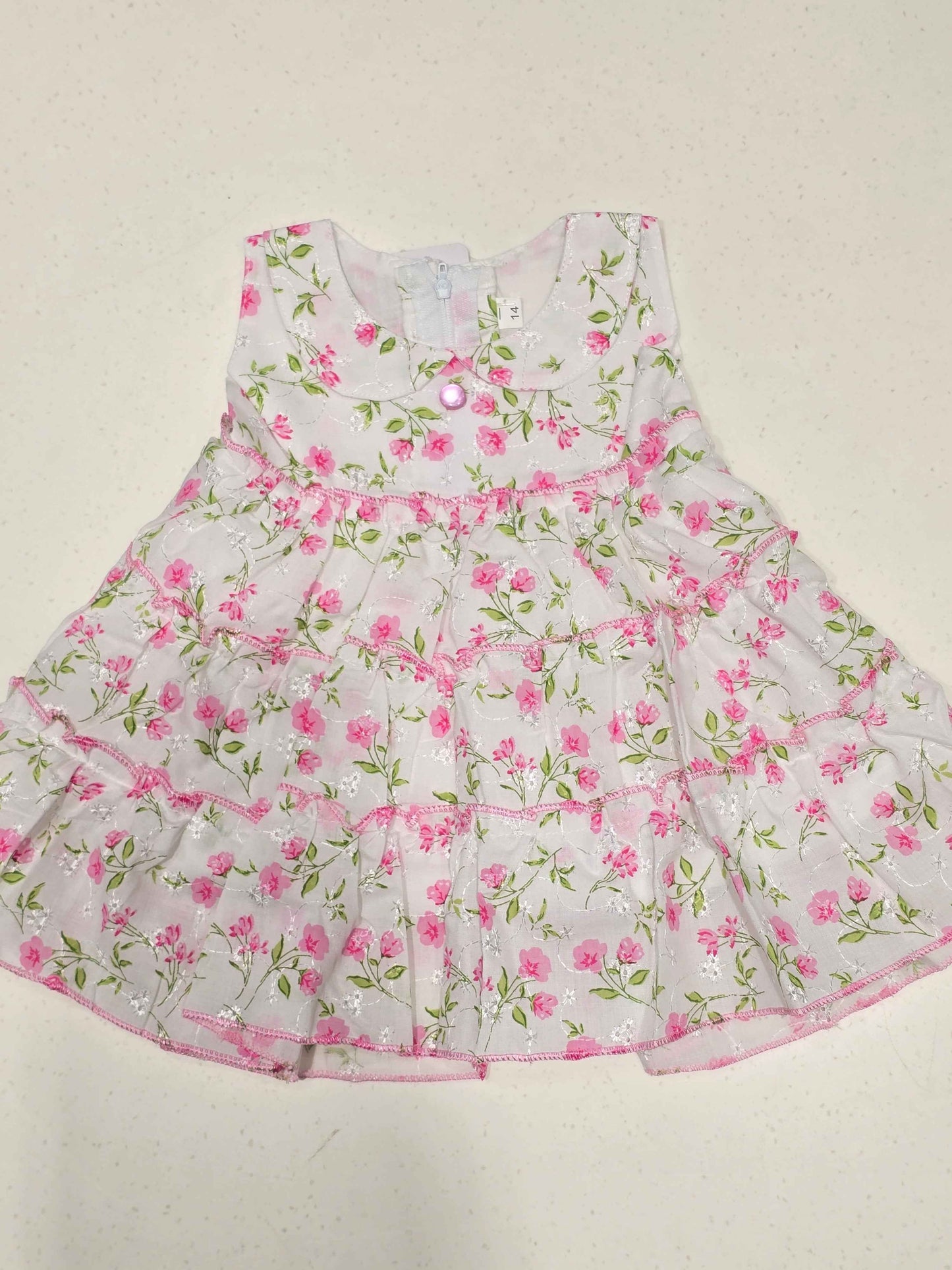 white baby girl's cotton frock dress featuring a vibrant pink floral print distributed in distinct tiered ruffle layers.